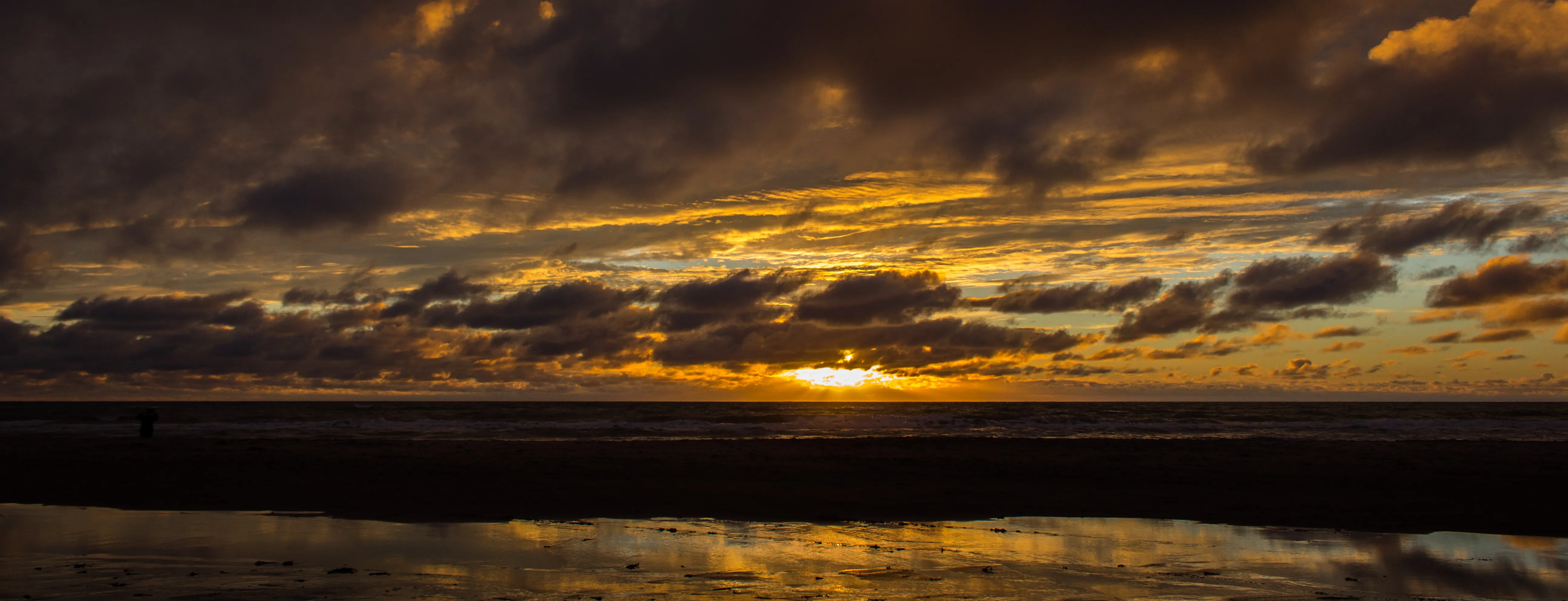 A sunset at a beach with some clouds in the sky